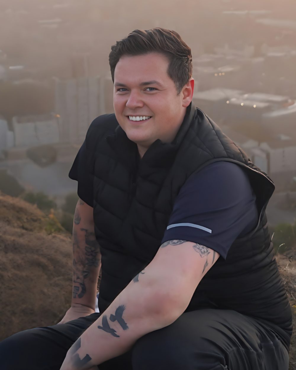 Carver Johnson smiling, sitting on a hillside above a city at sunset